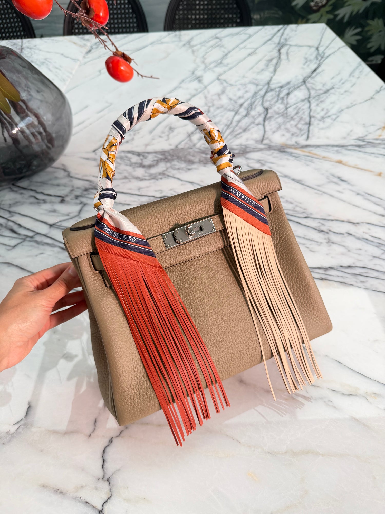 Beige handbag with orange fringes and colorful strap on a marble surface